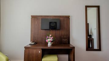 Ett skrivbord i trä, ett tv-apparatskärm, en vas med blommor och en spegel på väggen.