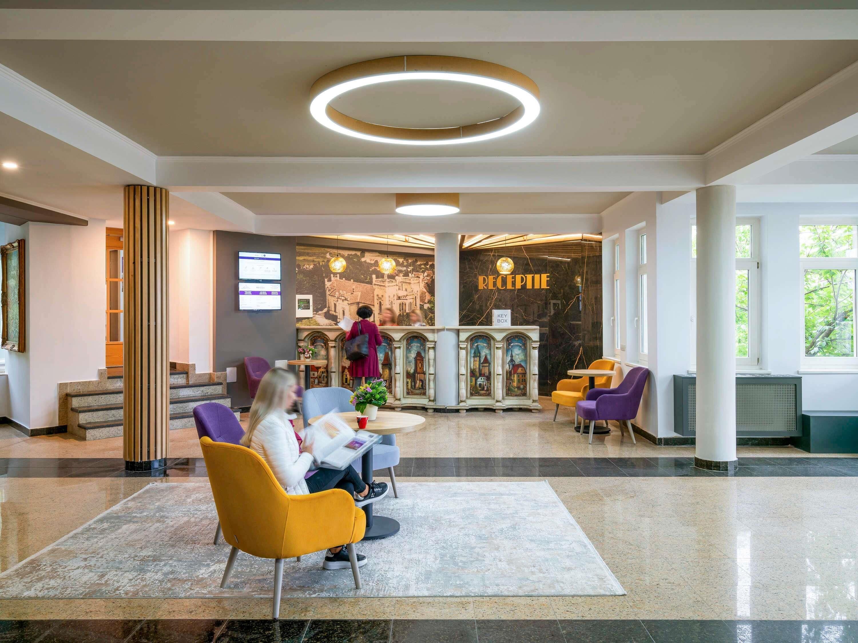 Zona de recepción de un hotel con piso de mármol, mostrador de recepción y arreglos de asientos.