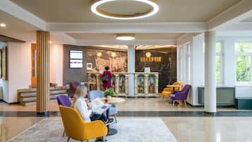 Zona de recepción de un hotel con piso de mármol, mostrador de recepción y arreglos de asientos.