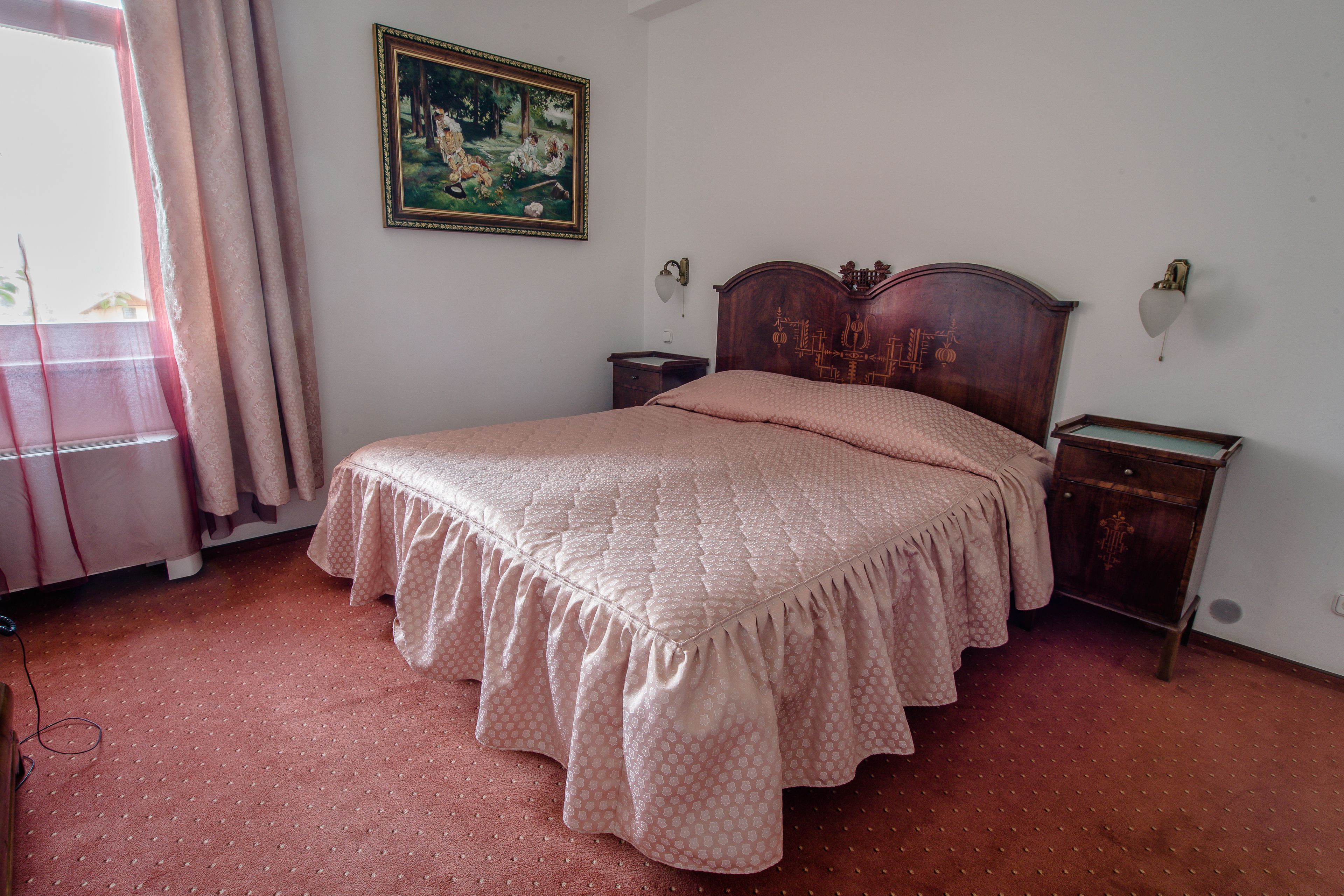 A bedroom with a bed, a nightstand, a dresser, a painting on the wall, and a window with curtains.