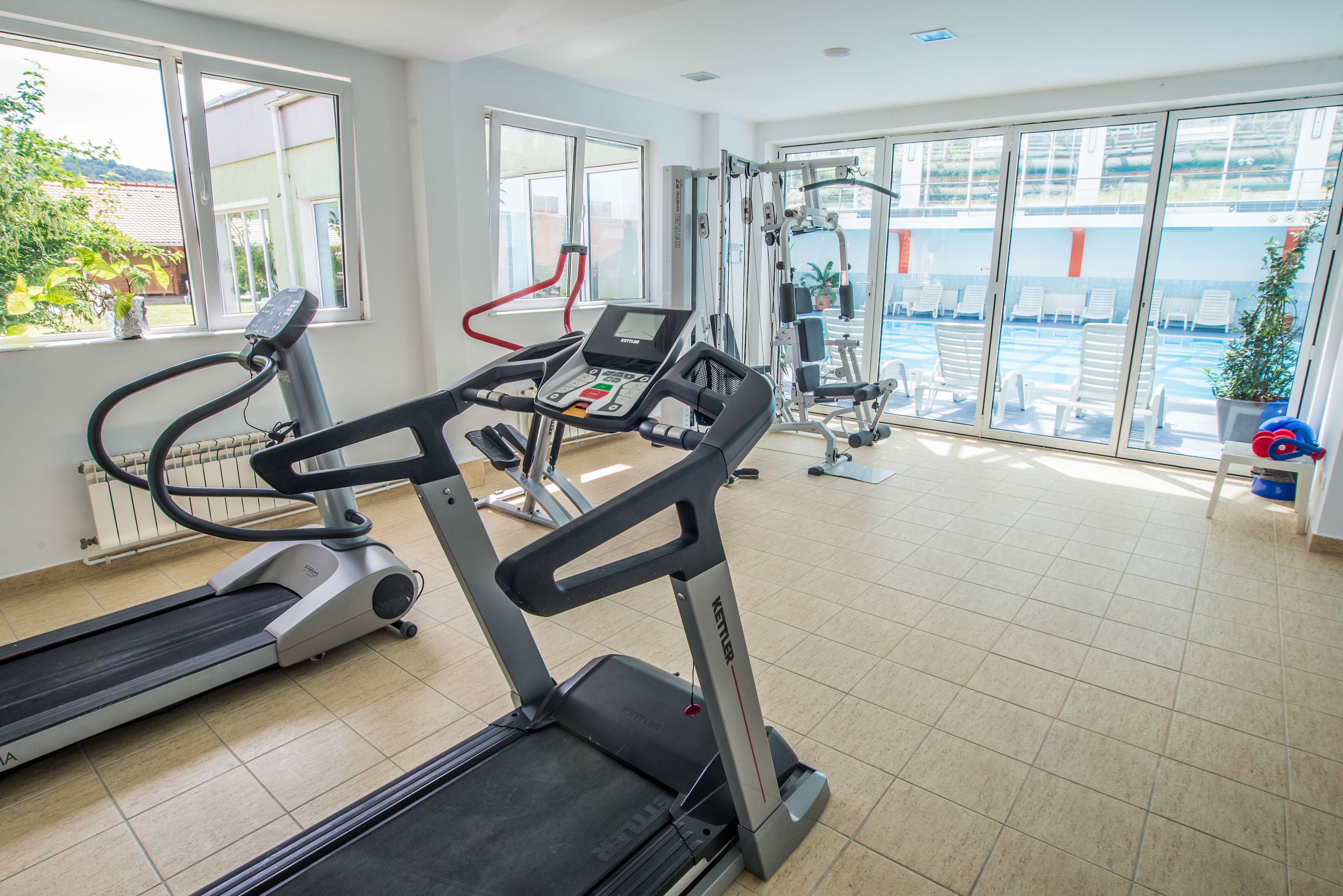A gym with treadmills, exercise machines, and large windows offering views of the outdoors.