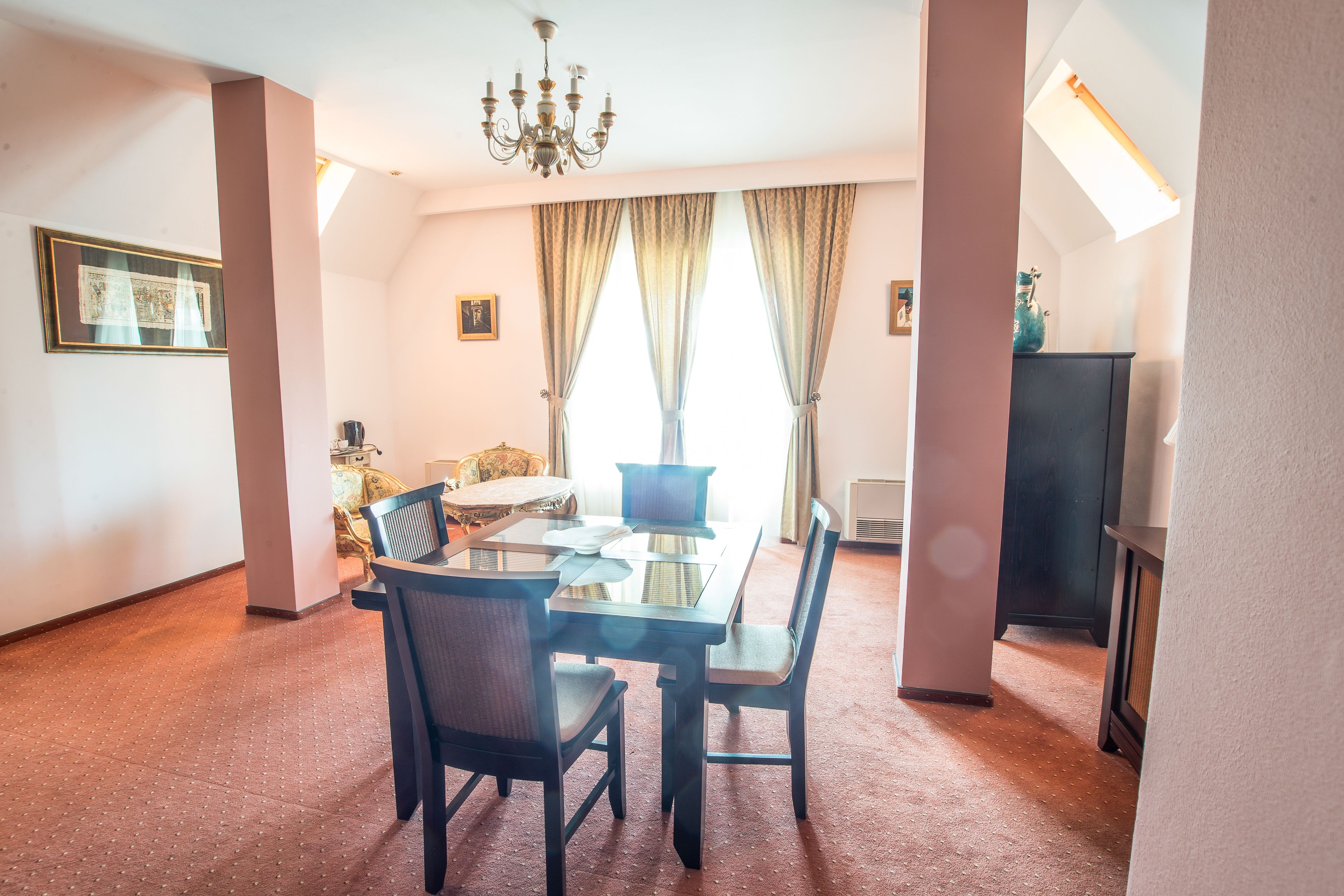 A dining area with a glass table and chairs, a chandelier, and a view of a living room with a sofa and a TV.