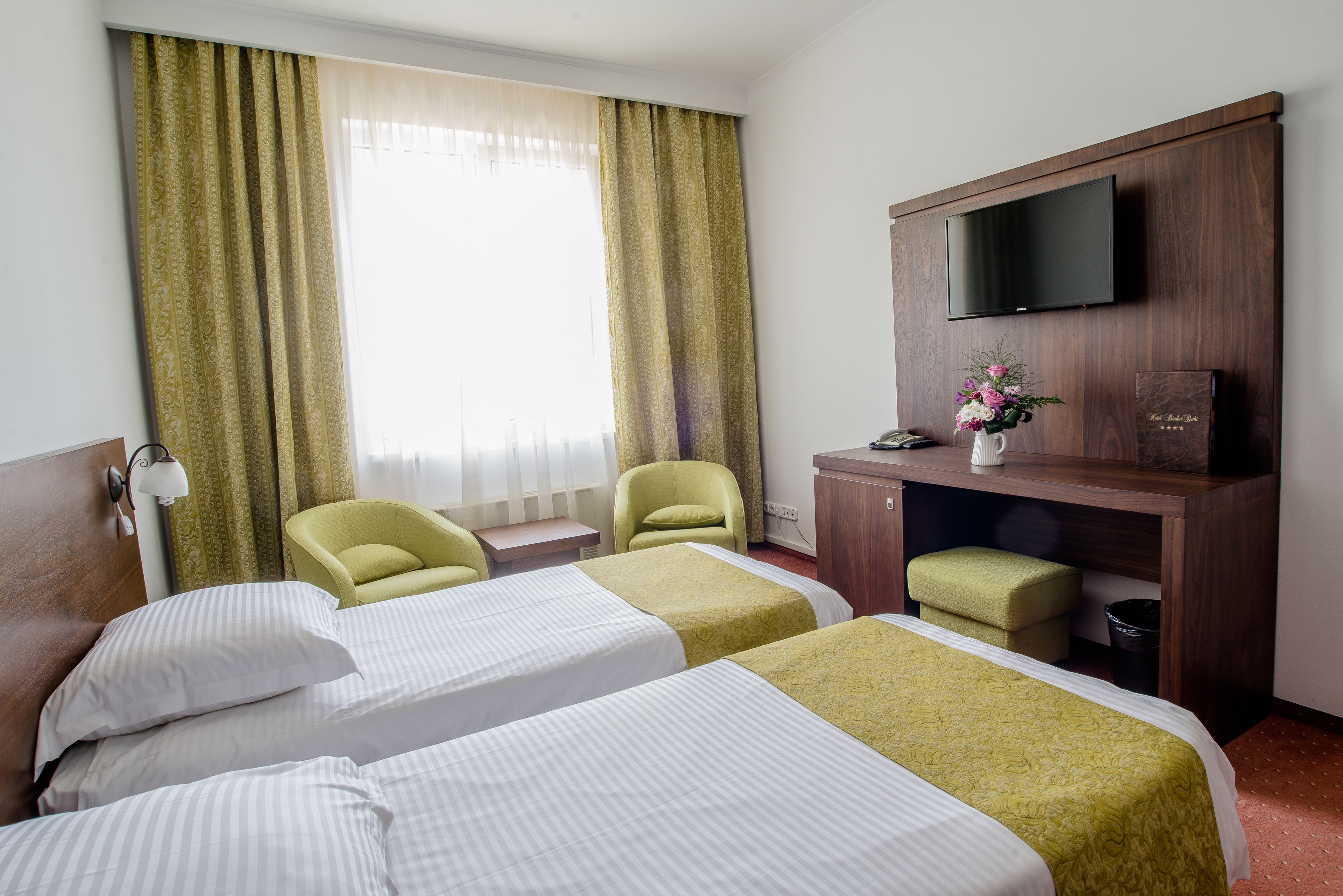 Een hotelkamer met twee bedden, een bureau, een televisie en een raam met gordijnen.