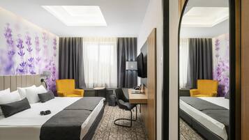 A hotel room with a bed, a desk, a chair, a TV, and a large mirror.