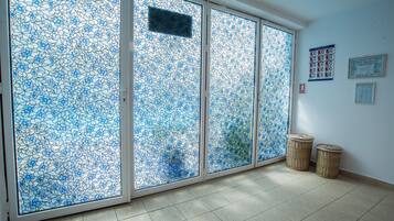 Una habitación con un amplio ventanal corredero de diseño floral azul, dos cestas de mimbre en el suelo y una pared con carteles informativos.