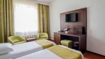 Habitación de hotel con dos camas, un escritorio, televisión de pantalla plana, una silla y una mesita.