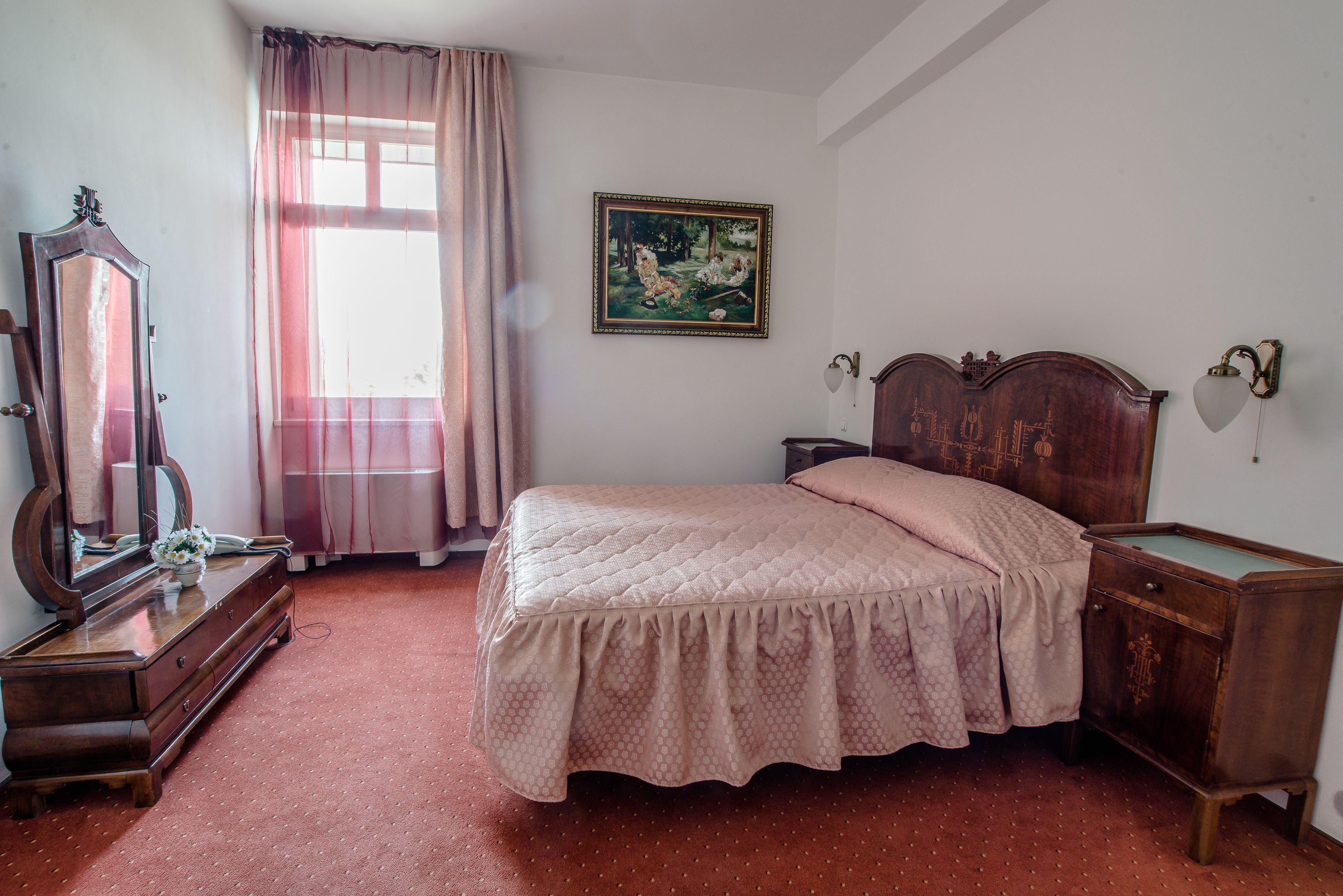 A bedroom with a wooden bed, a dresser, a mirror, and a painting on the wall.