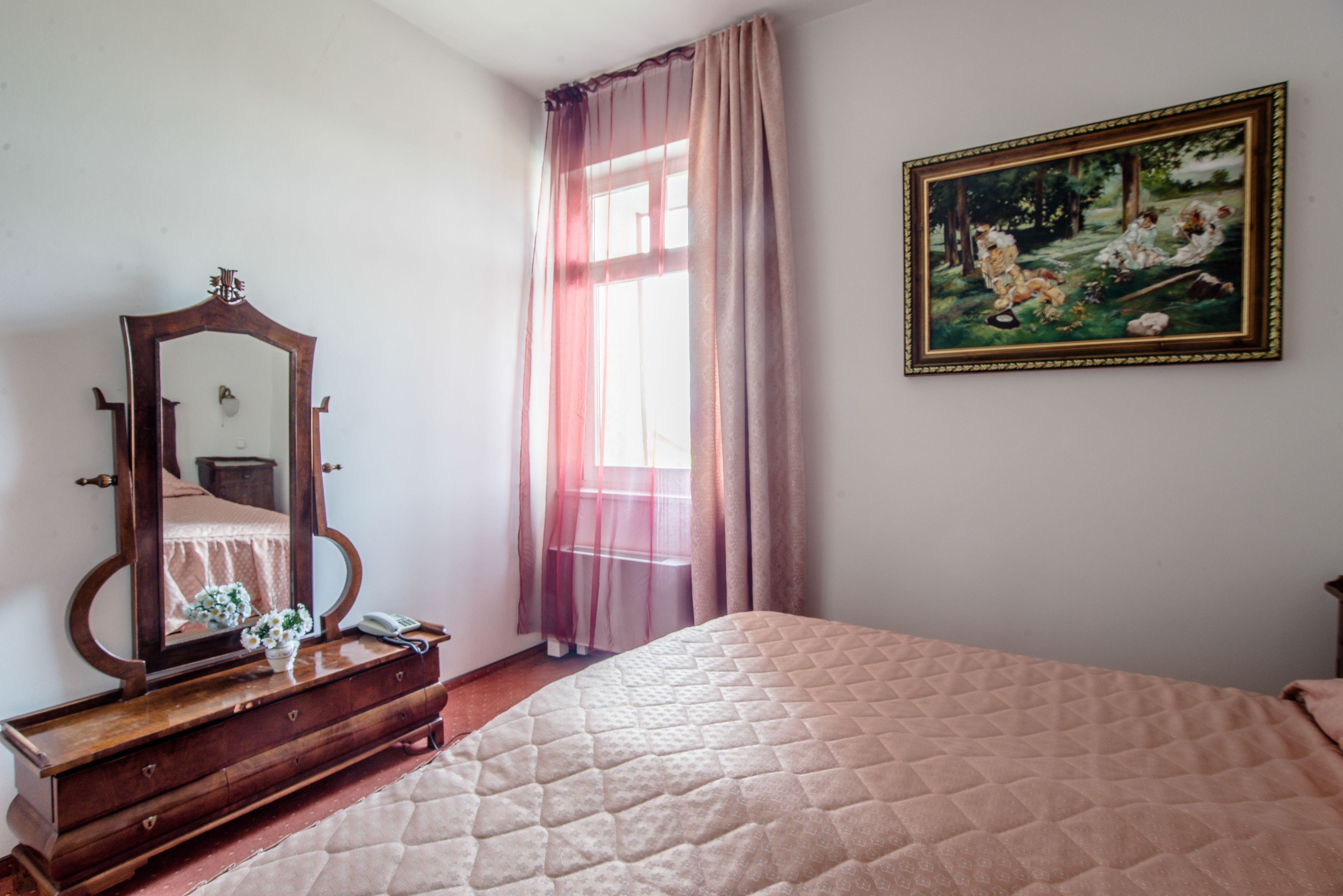 Un dormitorio con una cama, un aparador, un espejo, un cuadro y una ventana con cortinas.