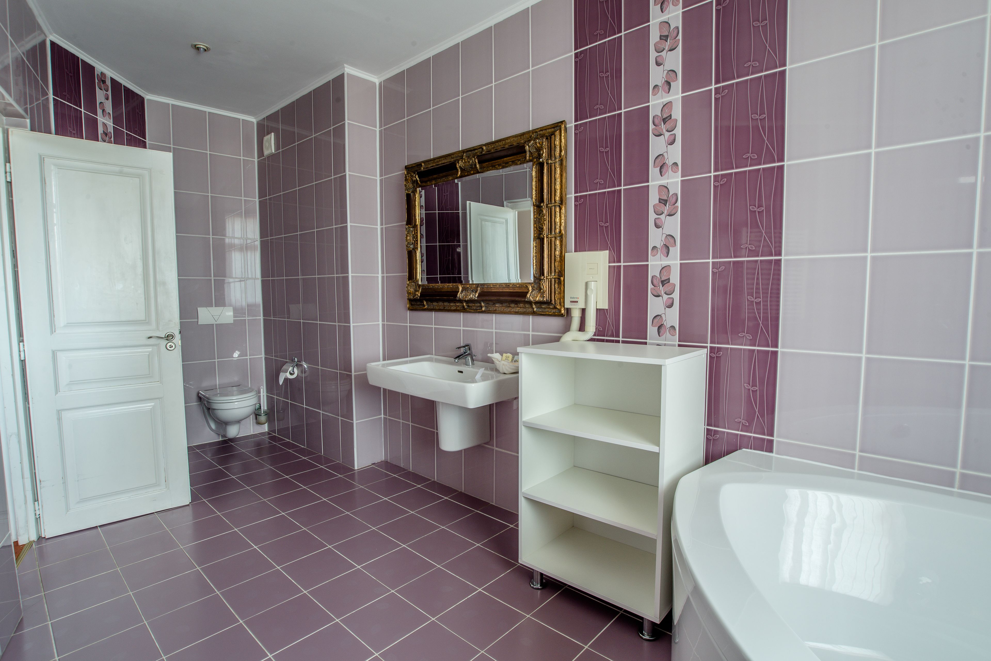 A bathroom with a white door, a sink, a mirror, and a bathtub.
