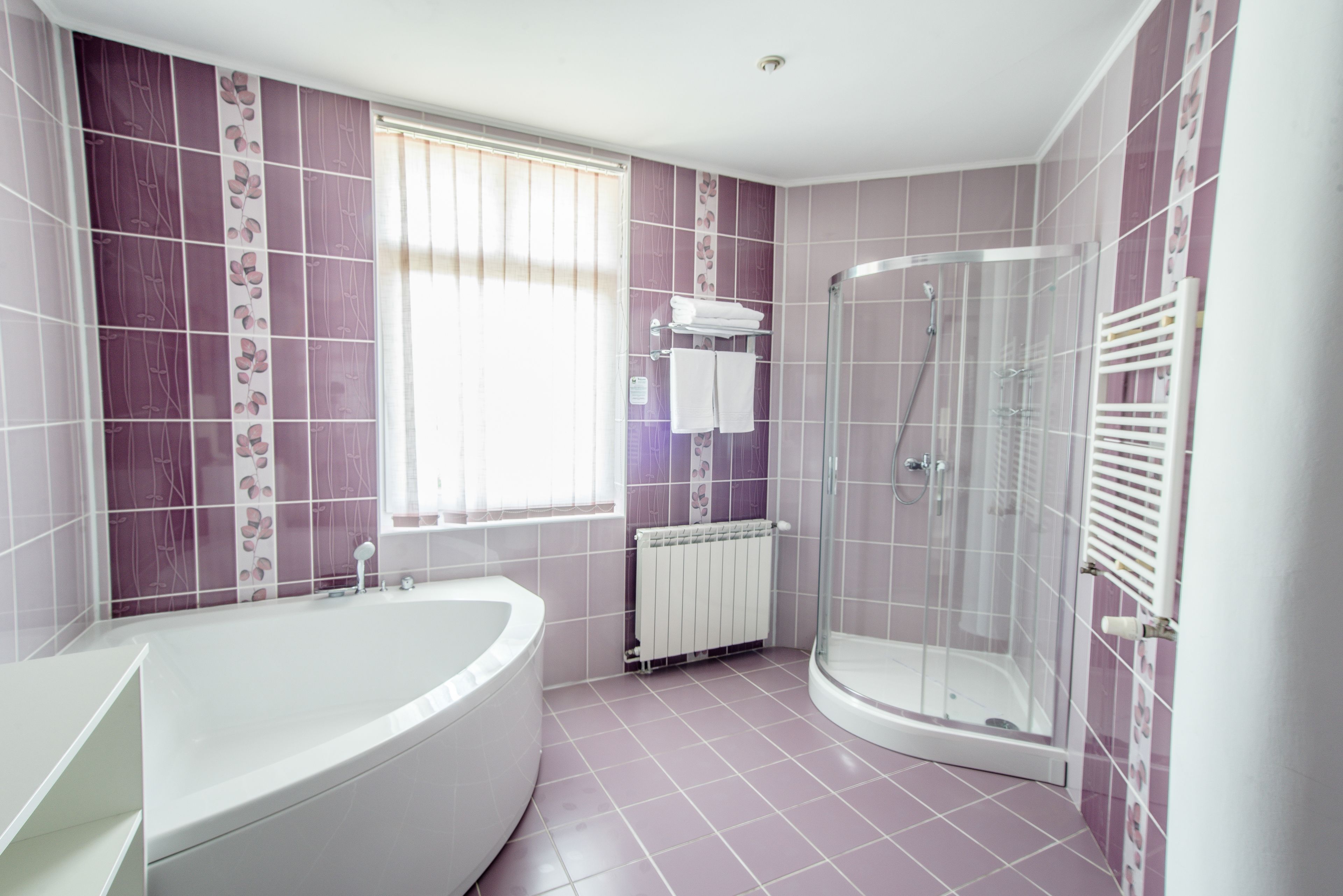 A bathroom with a bathtub, a glass-enclosed shower, and a window with blinds.