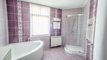 A bathroom with a bathtub, a glass-enclosed shower, and a window with blinds.