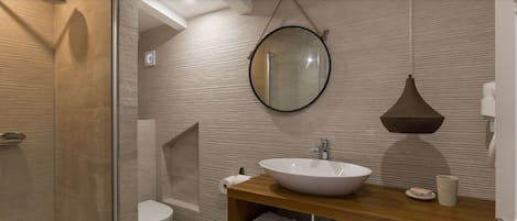 A modern bathroom with a glass shower enclosure, a white sink, and a round mirror.
