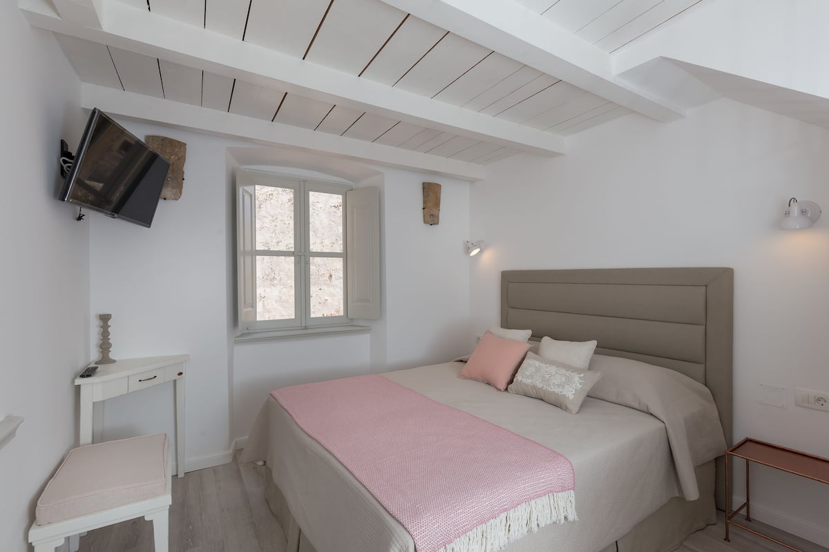 A bedroom with a bed, bedside table, and a window.