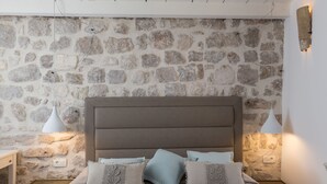 A bedroom with a stone wall, a bed with multiple pillows, bedside tables, and wall-mounted lamps. - Dubrovnik Sweet House (Dubrovnik)