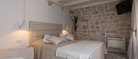 A bedroom with a stone wall, a bed with a headboard, a bedside table, a lamp, and a wall-mounted TV.