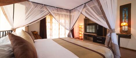 A bedroom with a canopy bed, a television, and a nightstand with a lamp.