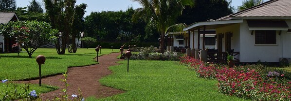A pathway leading to a white building with a porch, surrounded by well-maintained grass and flowering plants.