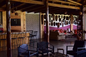 A spacious lounge area with wooden furniture, a bar with stools, and a wall adorned with various masks.