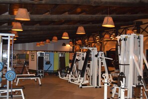 A gym with various exercise equipment, wooden beams on the ceiling, and hanging lamps.