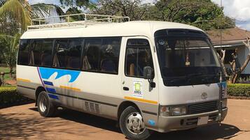 A white van with blue and yellow stripes parked on a dirt road, surrounded by trees and a building in the background.