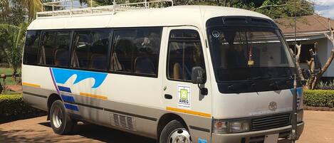 A white van with blue and yellow stripes parked on a dirt road, surrounded by trees and a building in the background.
