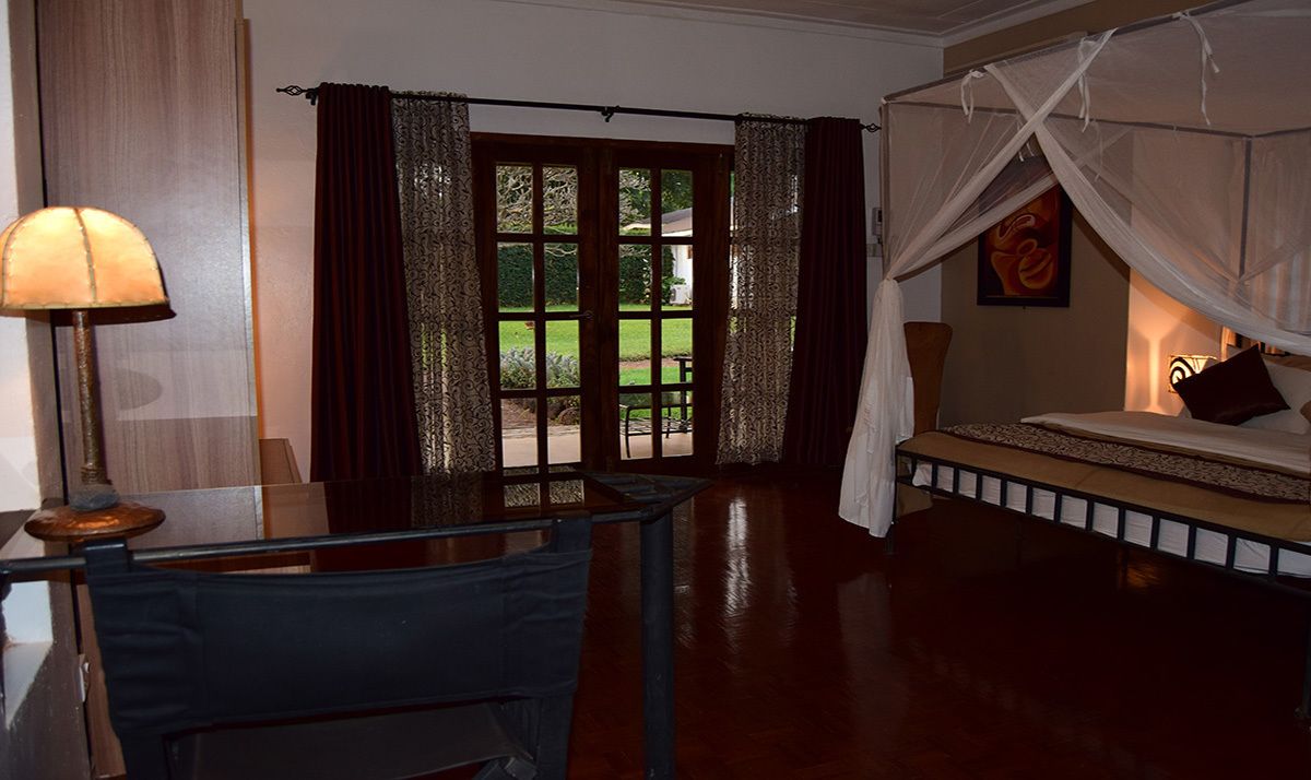 A room with a bed under a canopy, a desk with a lamp, and a view of the outdoors through a glass door.