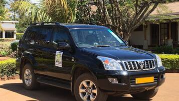 Un SUV negro estacionado en un área pavimentada, con un edificio y árboles al fondo.