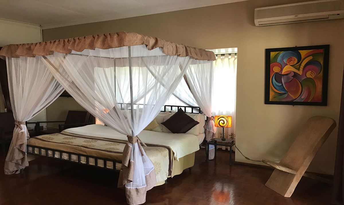 Una stanza con un letto a baldacchino, un comodino con una lampada, una sedia e un quadro colorato appeso al muro.