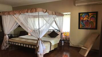 Una stanza con un letto a baldacchino, un comodino con una lampada, una sedia e un quadro colorato appeso al muro.