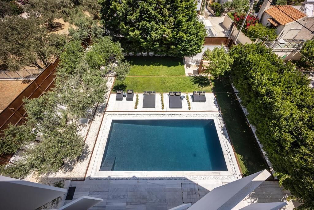 Una piscina rettangolare con un solarium circostante, immersa tra alberi e un piccolo prato.