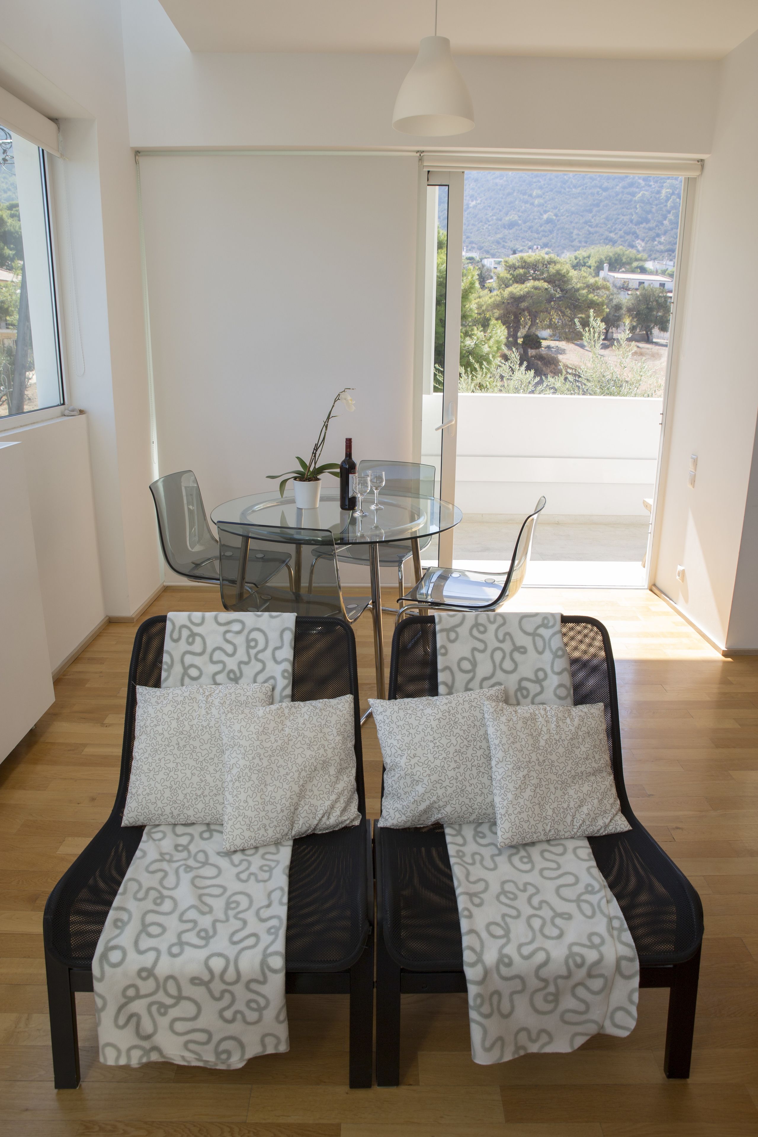 A dining area with a glass table and chairs, a potted plant, and a bottle of wine.