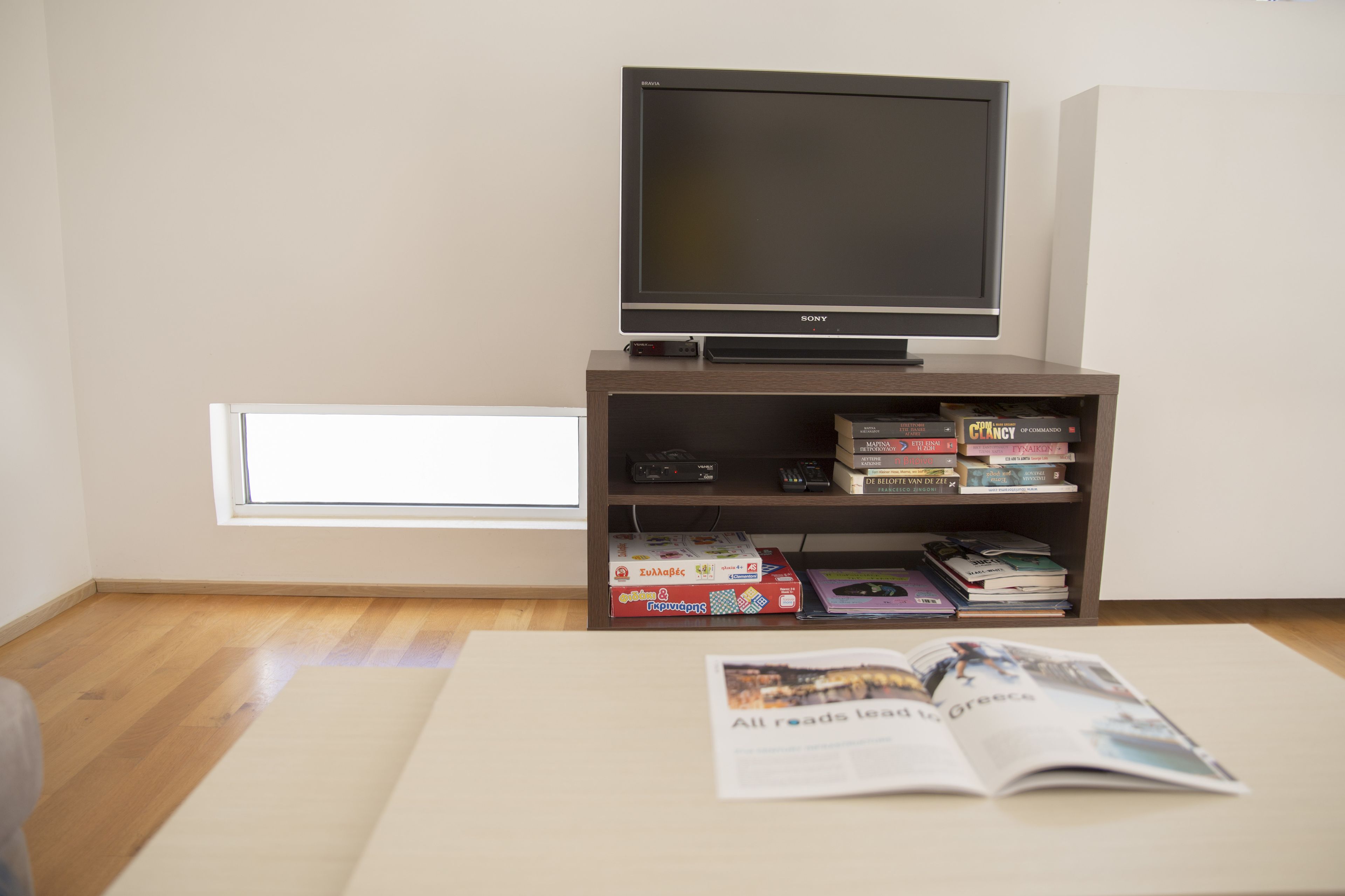 A room with a television on a wooden stand, a bookshelf with books and a DVD player, and a window providing natural light.