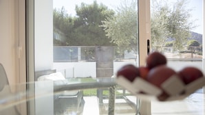 Un balcon doté d’une balustrade en verre, offrant une vue sur des arbres et un immeuble, ainsi qu’une table sur laquelle se trouve un panier de fruits.