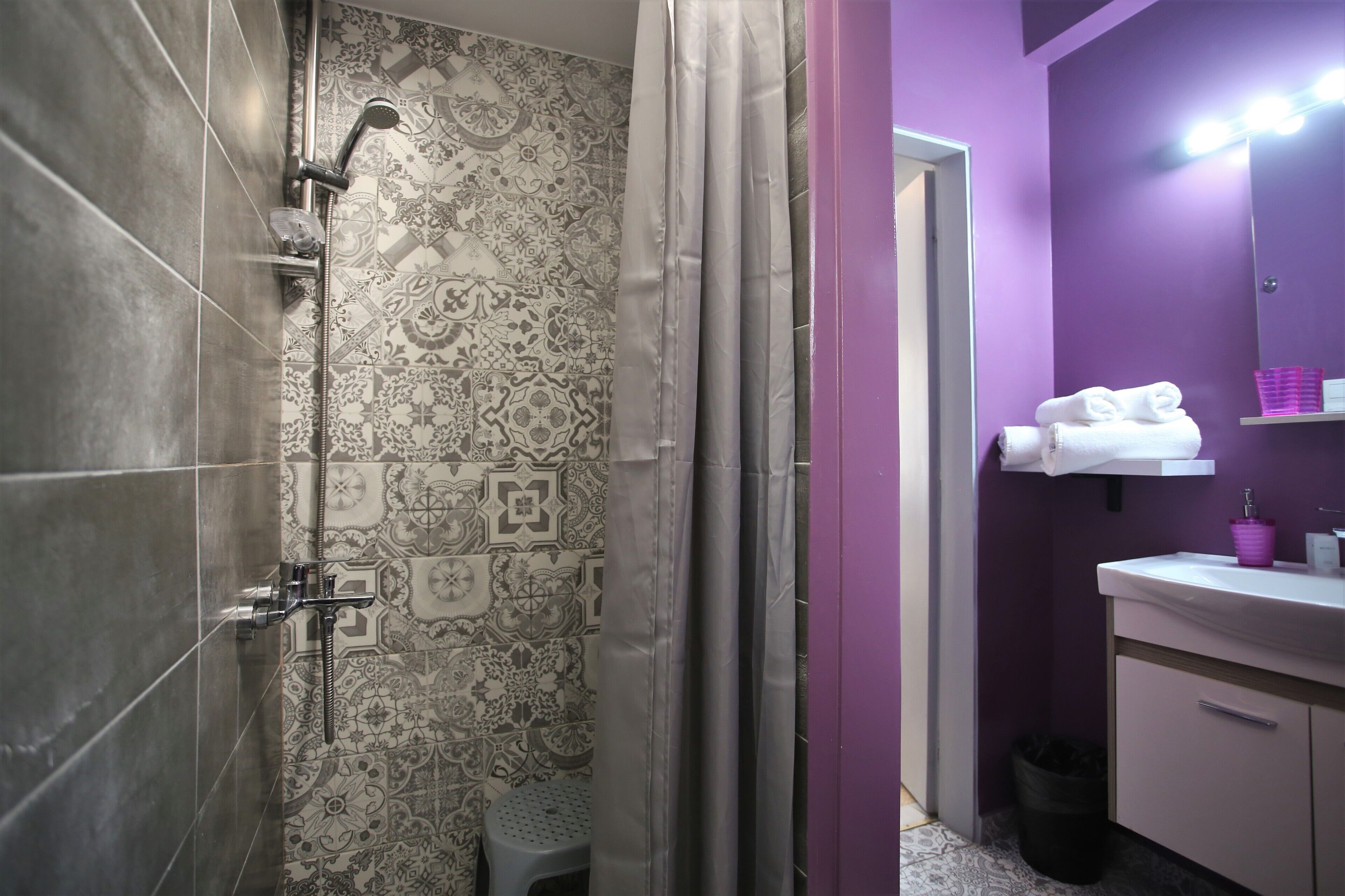A bathroom with patterned tiles, a shower with a handheld showerhead, a toilet, and a vanity with a mirror and shelves.