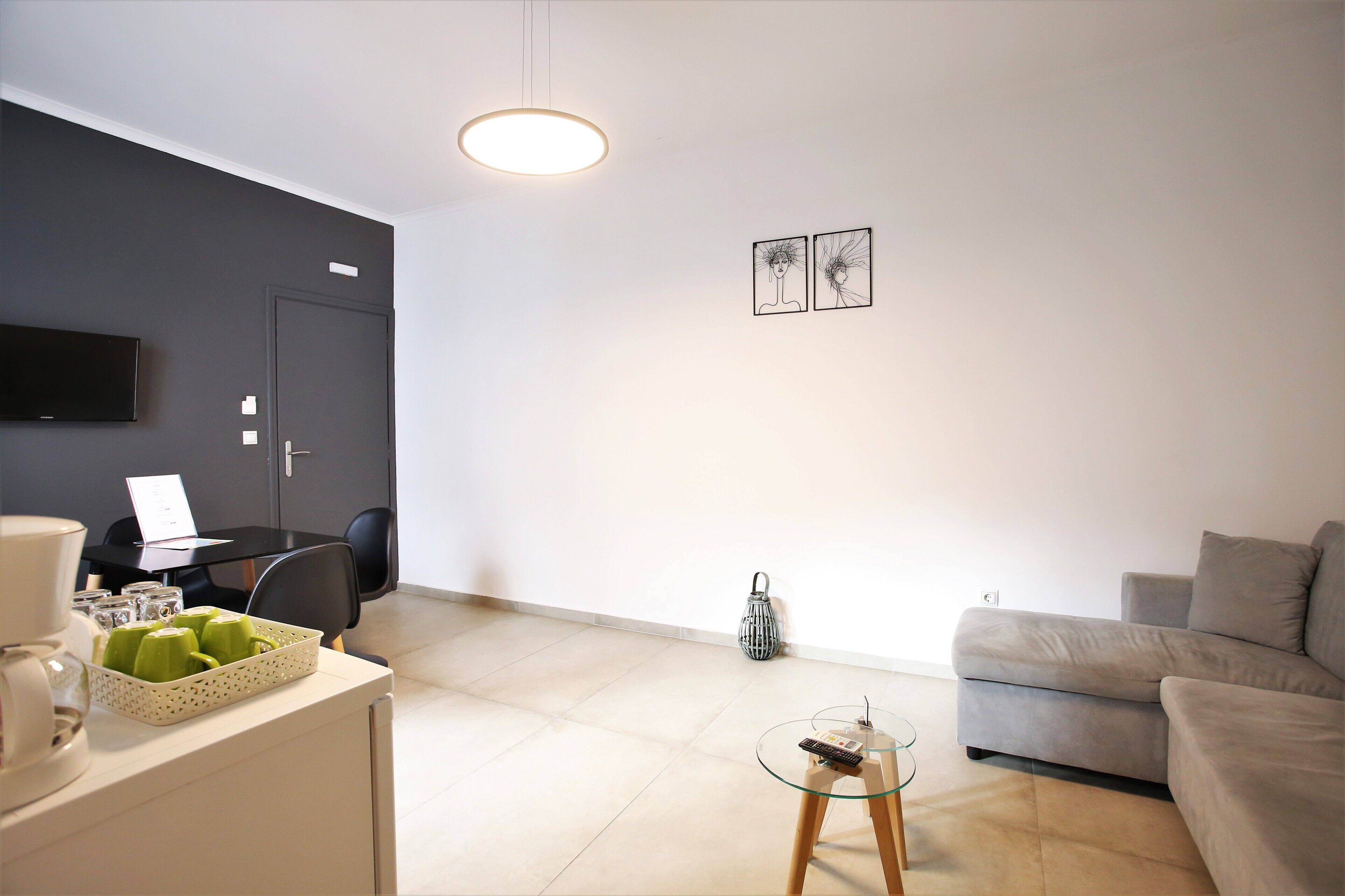 Un salon moderne avec un canapé gris, une table basse en verre, un téléviseur à écran plat fixé au mur et un coin repas comprenant une table et des chaises.
