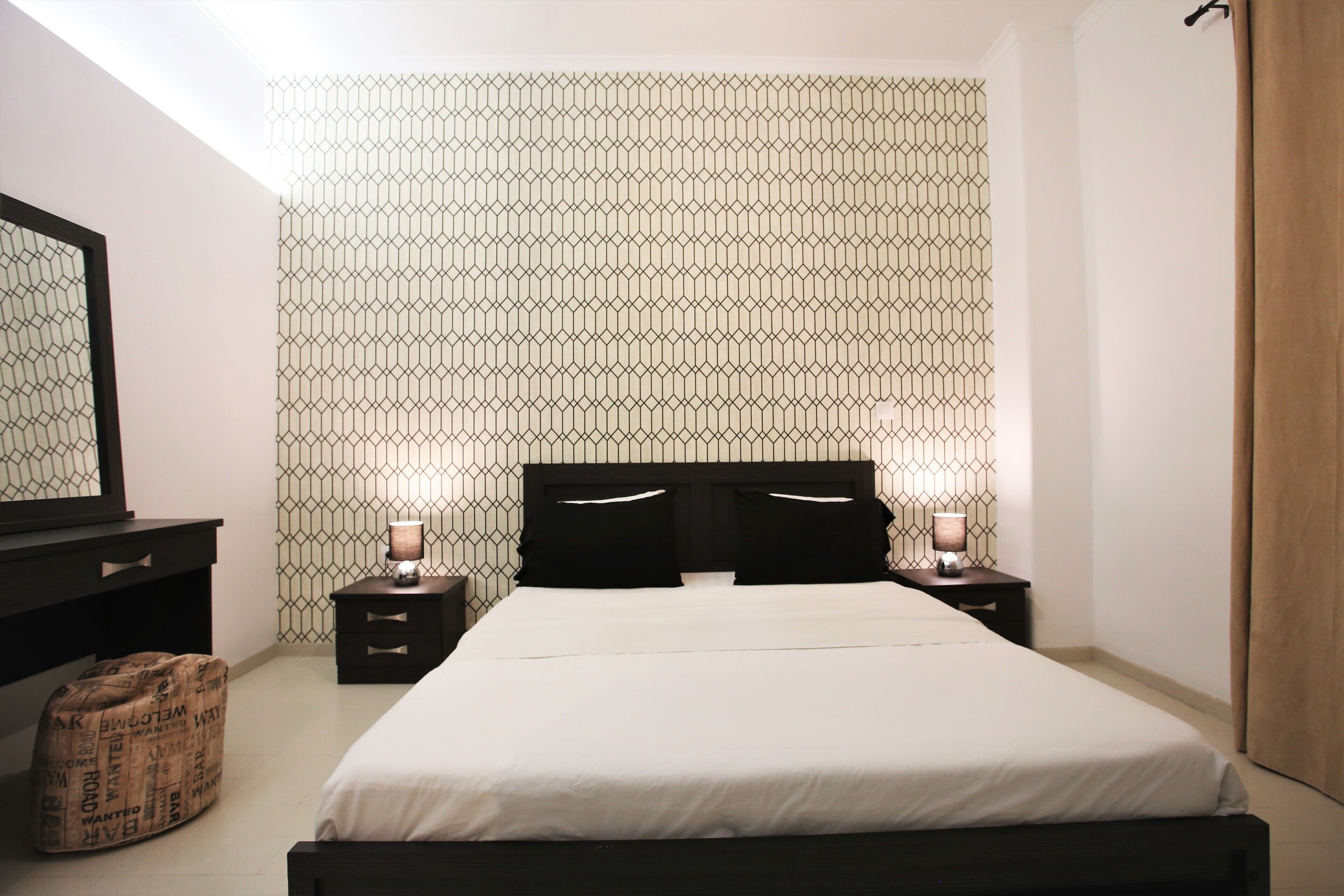 A bedroom with a bed, bedside tables, a mirror, and a patterned wall.