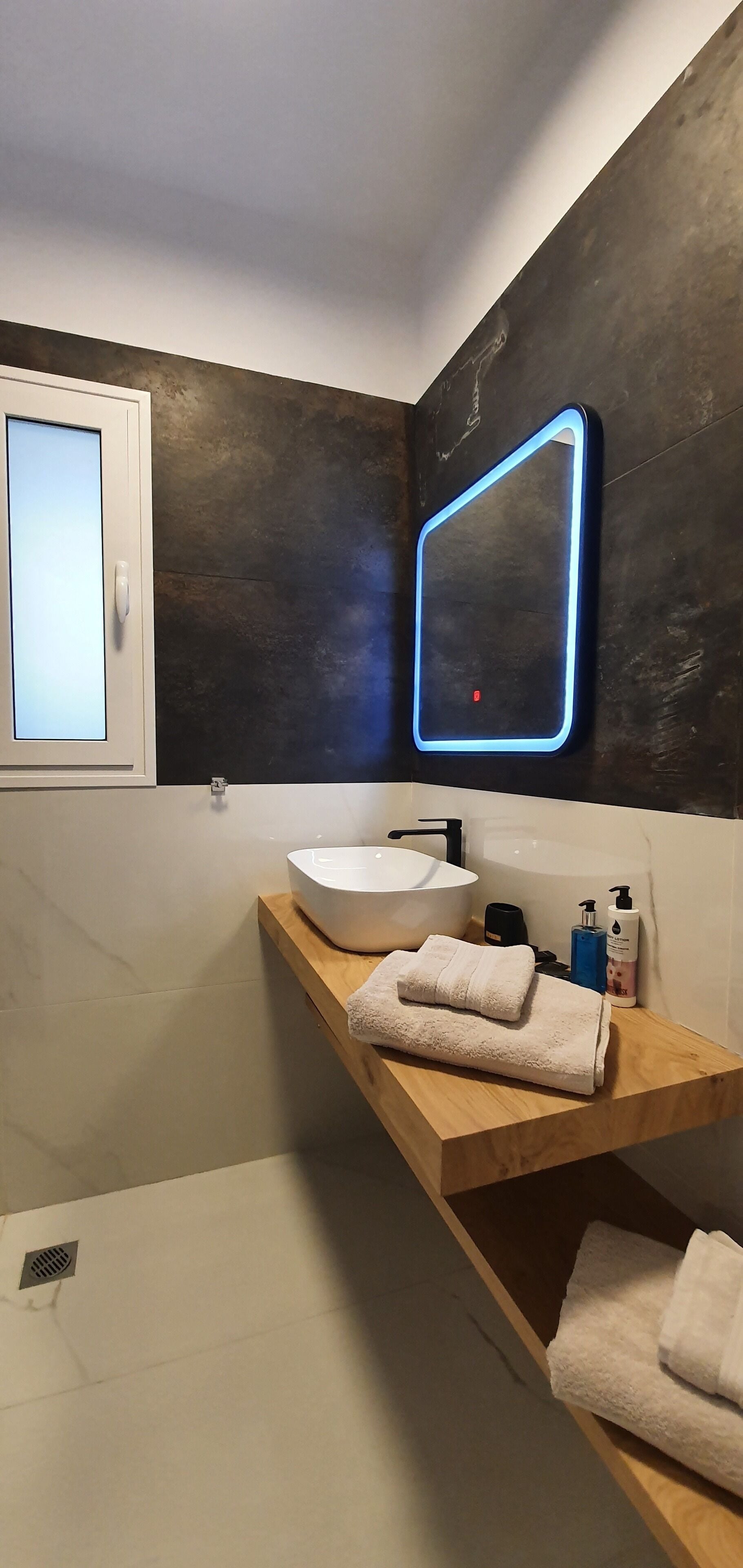A modern bathroom with a large mirror, a white sink, and a wooden vanity.