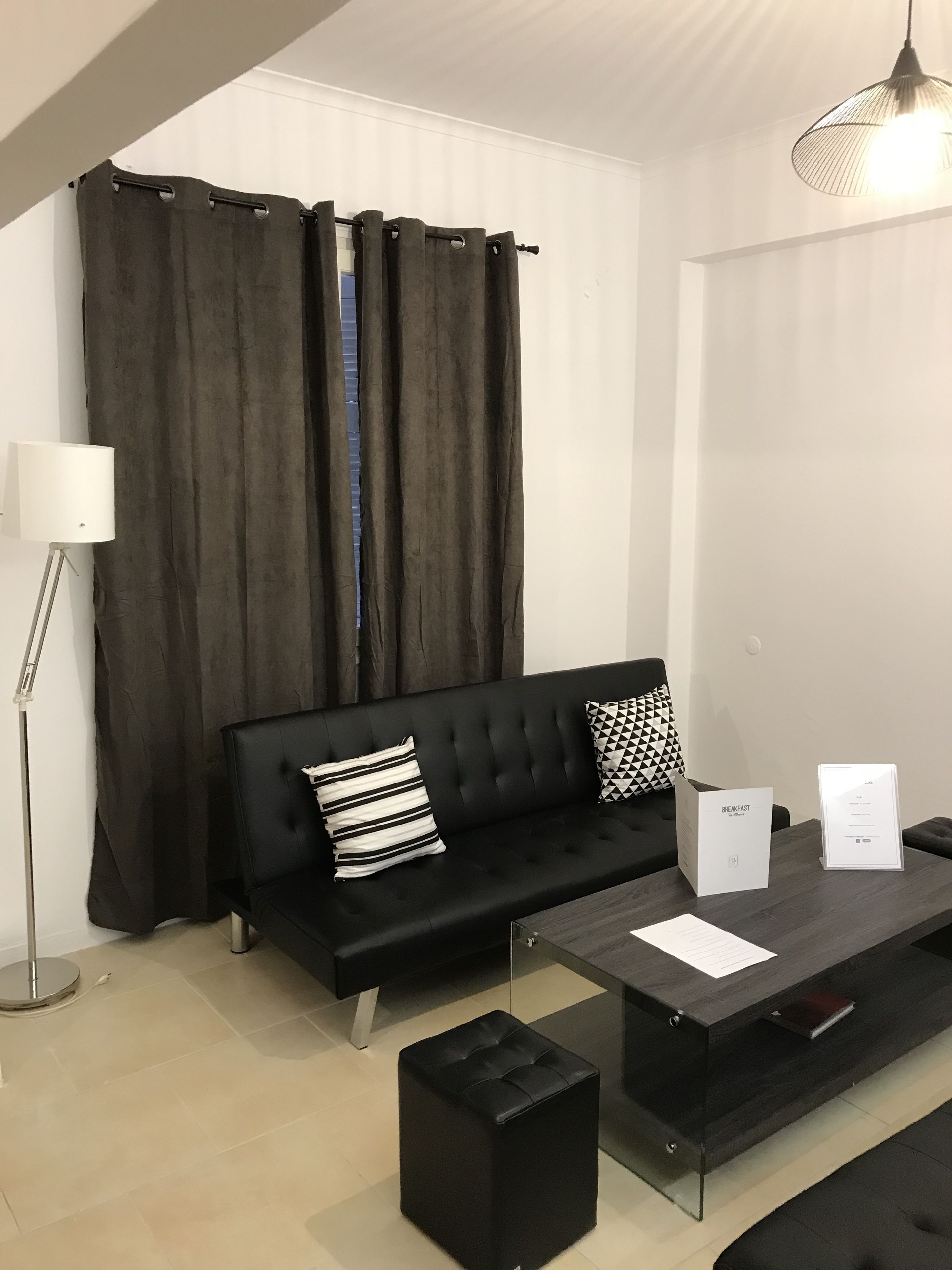Una sala de estar moderna con un sofá negro, dos cojines, una mesita de centro y una lámpara de pie.