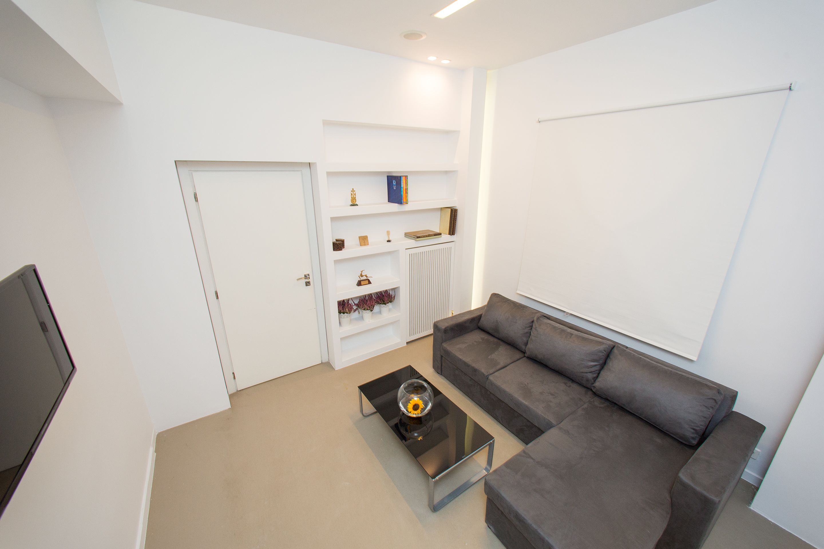 A modern living room with a grey sofa, a glass coffee table, and a white door.