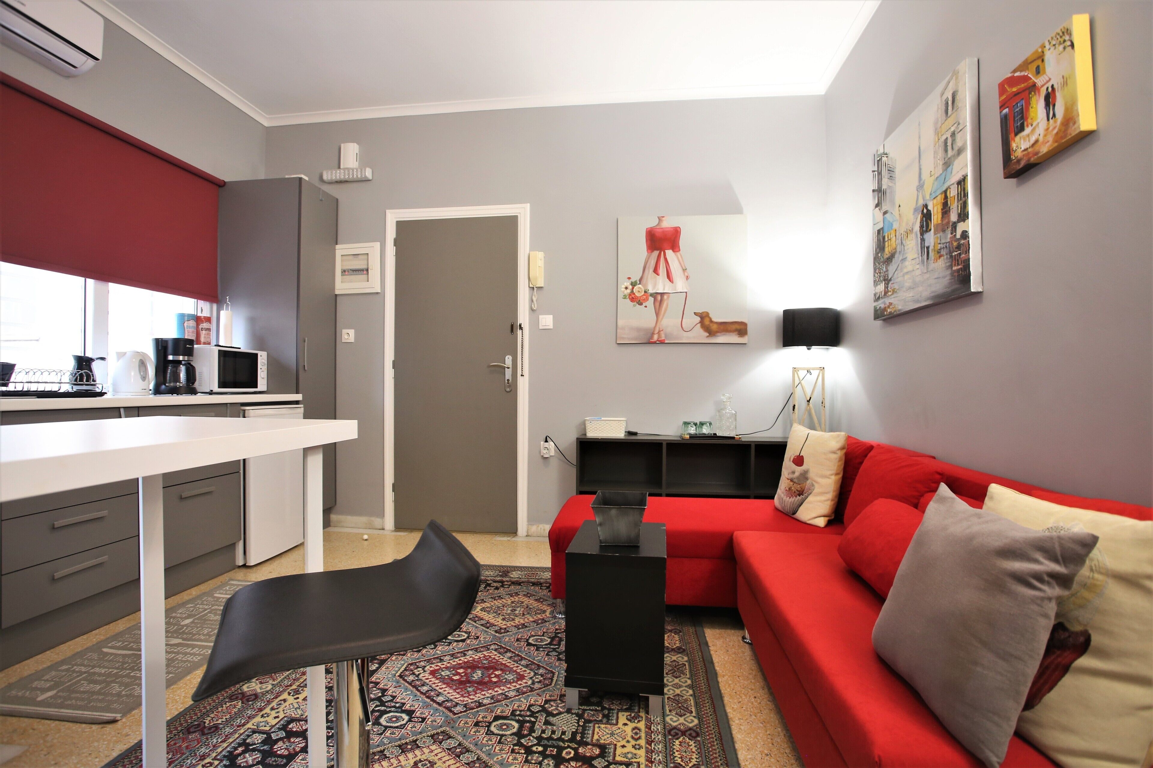 A compact living space with a kitchenette, a red sofa, a patterned rug, and artwork on the walls.