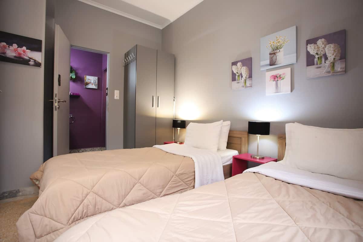 A hotel room with two beds, a wardrobe, a bathroom, and artwork on the walls.