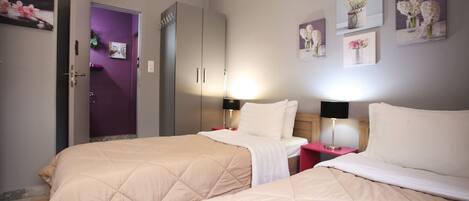 A hotel room with two beds, a wardrobe, a bathroom, and artwork on the walls.