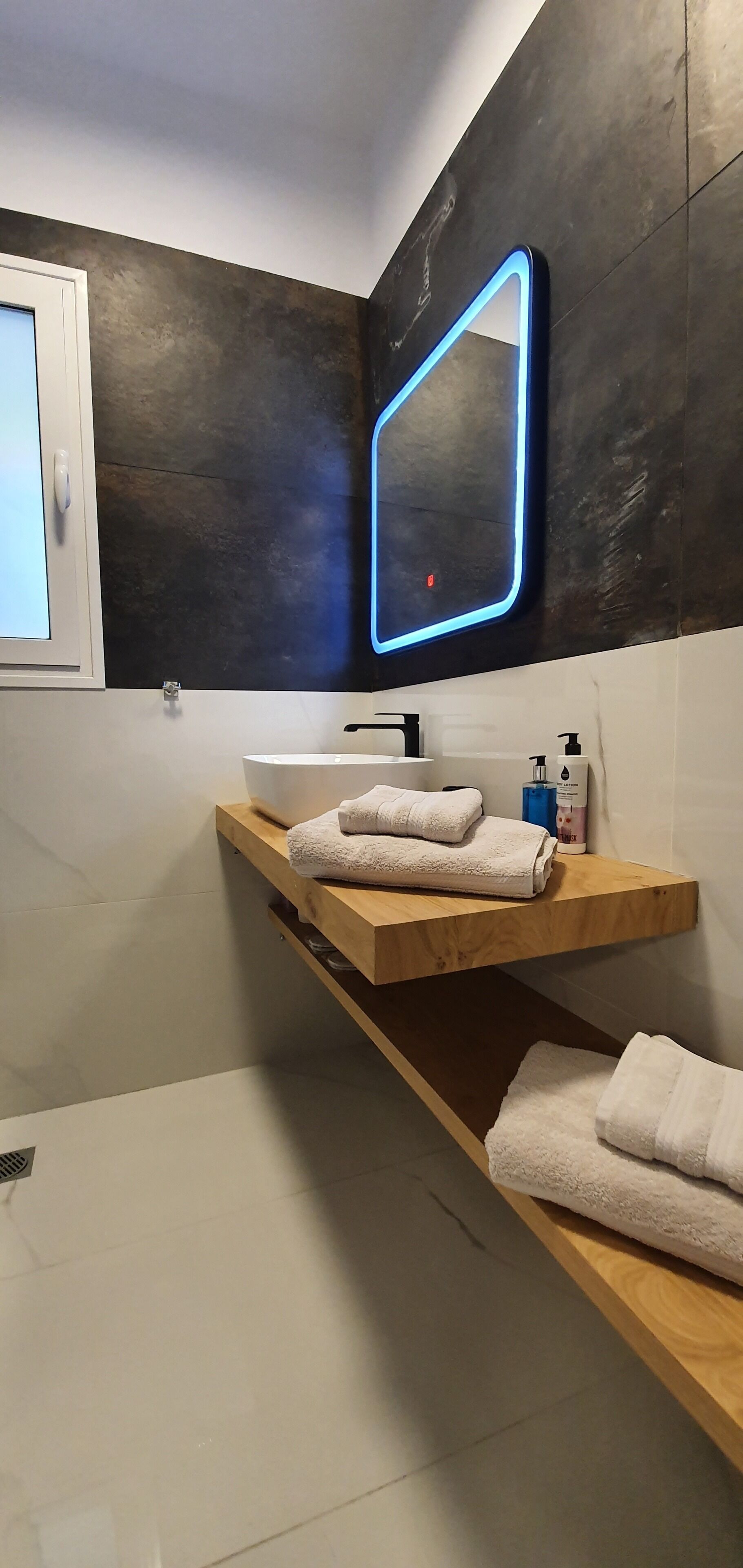A modern bathroom with a wooden vanity, a white sink, and a blue neon light above the mirror.