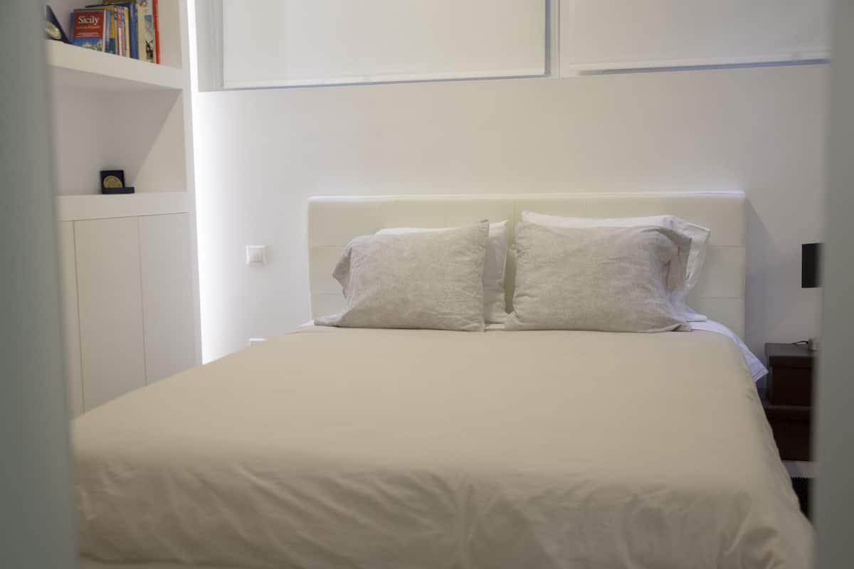 A neatly made bed with white bedding in a room with white walls and a white headboard.