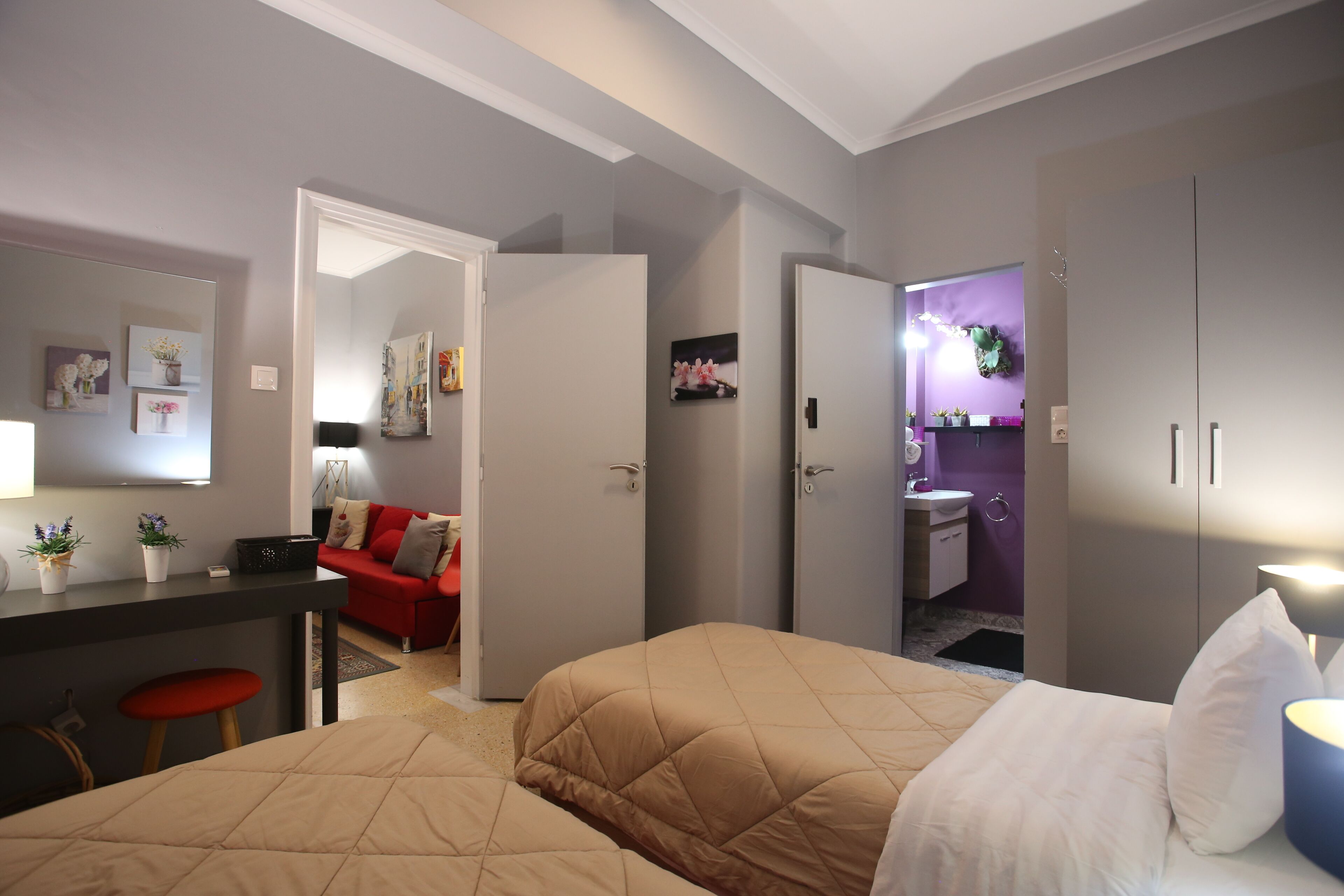 A hotel room with two beds, a desk, a red sofa, and a bathroom visible through an open door.