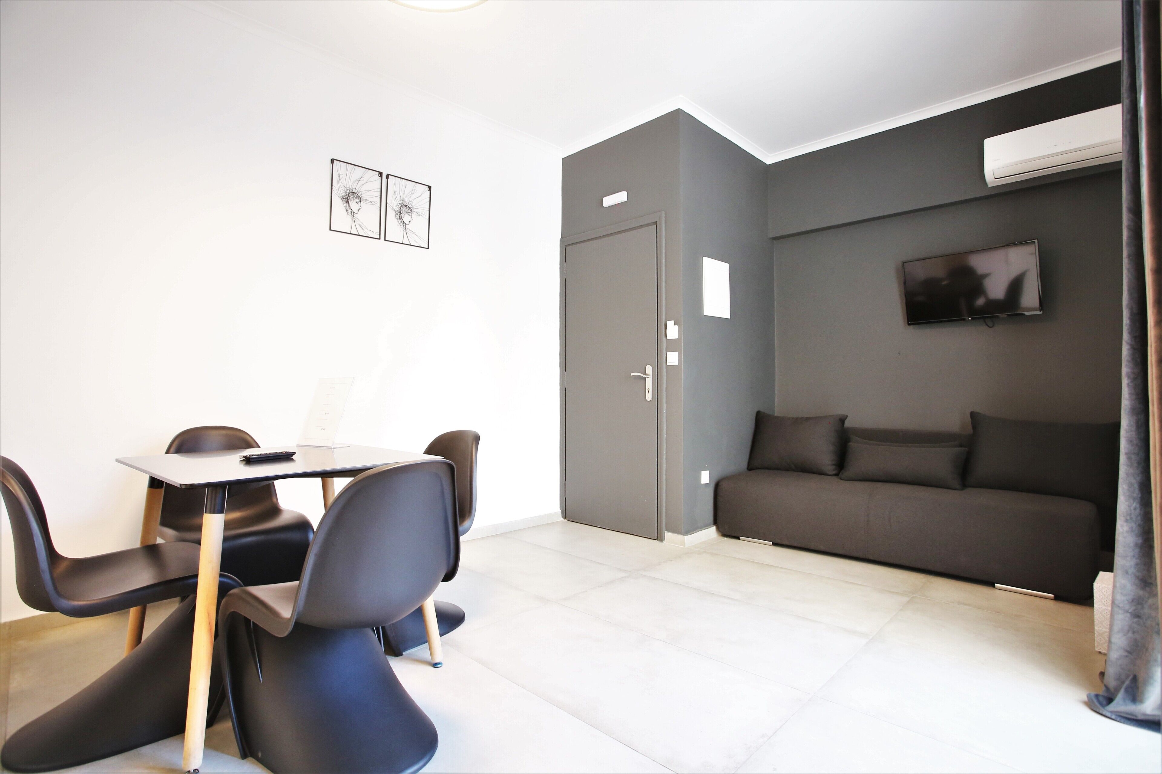 A modern living room with a grey sofa, a TV mounted on the wall, and a dining area with a table and chairs.