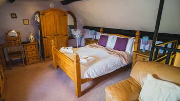 A bedroom with a wooden bed, a wooden wardrobe, a bedside table with a lamp, a chair, and a small table with a lamp.