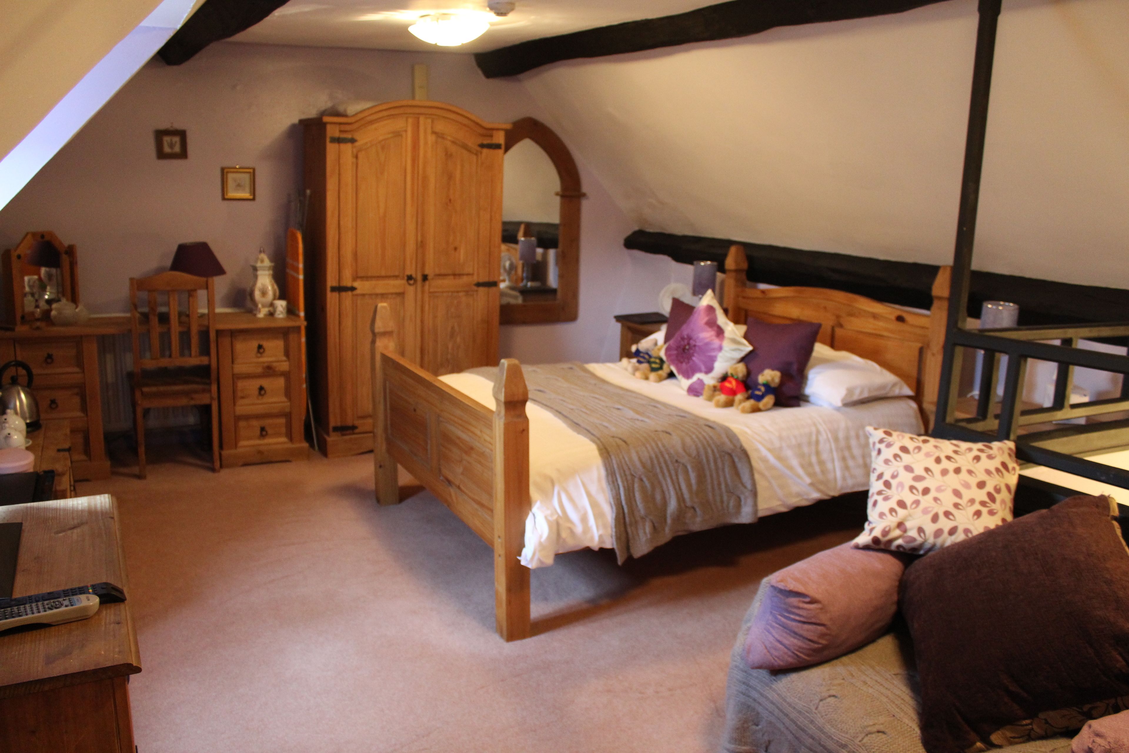 A bedroom with a wooden bed, a desk with a chair, a wardrobe, and a mirror.