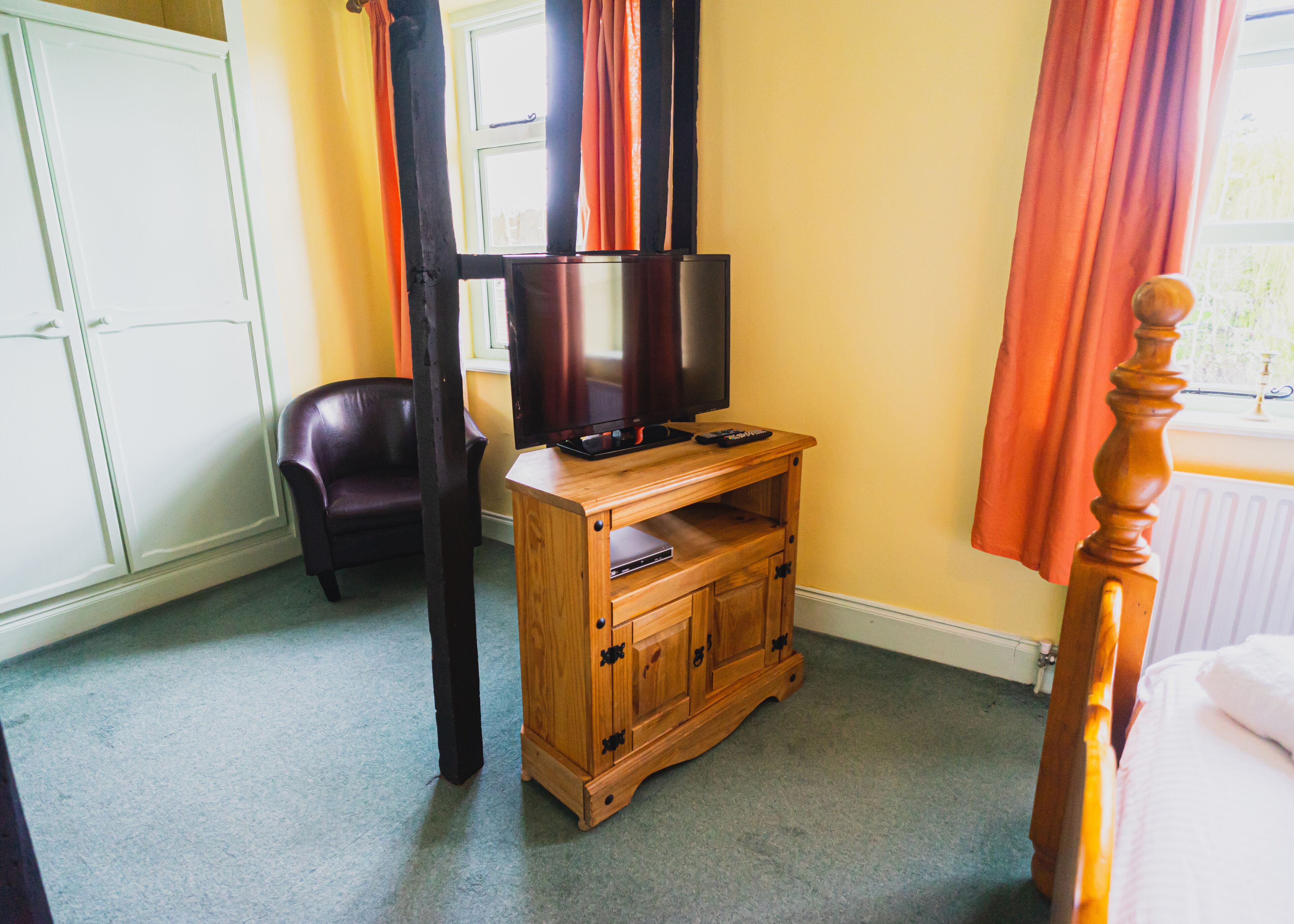 A room with a wooden TV stand, a leather chair, and a bed with a wooden headboard.