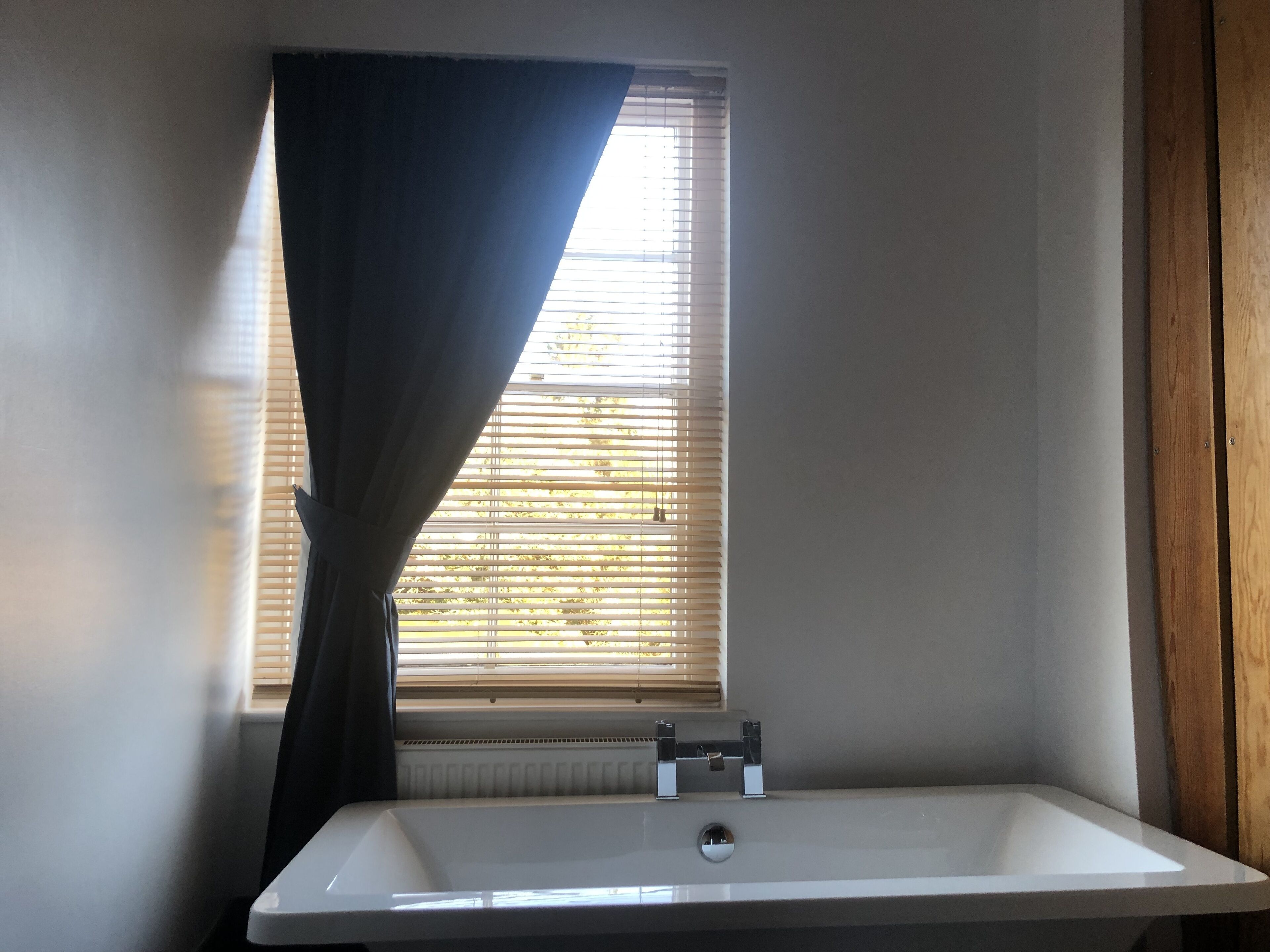 A bathroom with a white sink, a window with blinds, and a radiator.